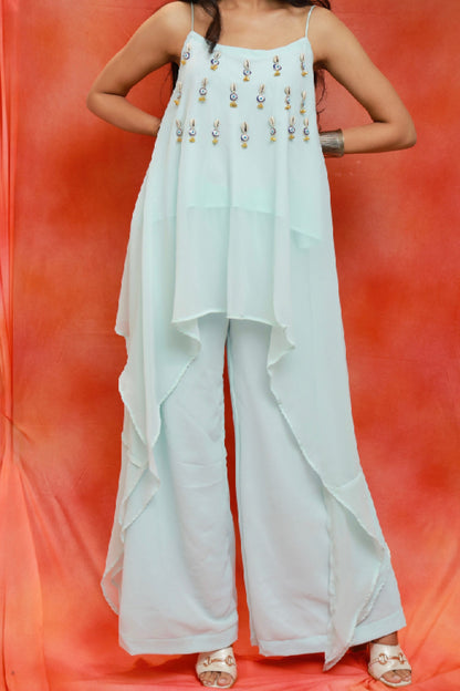 Model wearing the Nazar Ice Blue Shell Co-ord Set in premium georgette featuring shell and evil-eye embellishments, an asymmetrical layered camisole top, and matching wide-leg pants.