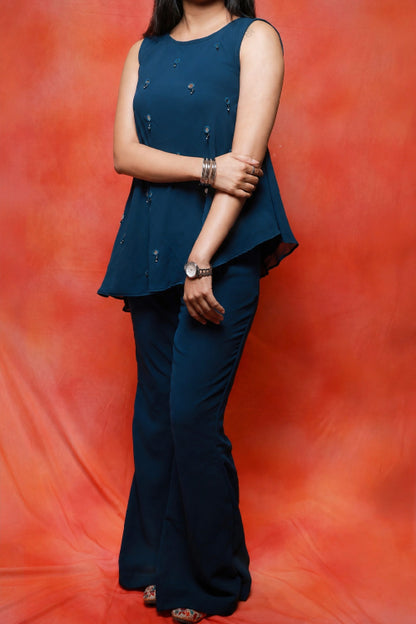 Model wearing the Nysa Teal Mirrorwork Co-ord Set in premium georgette featuring a sleeveless asymmetrical top with mirror work and matching flared pants.