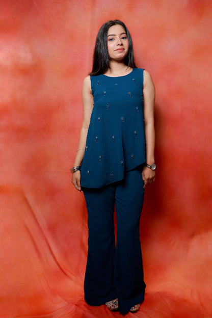 Model wearing the Nysa Teal Mirrorwork Co-ord Set in premium georgette featuring a sleeveless asymmetrical top with mirror work and matching flared pants.